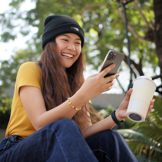 A woman sitting outside, holding a mug and phone.