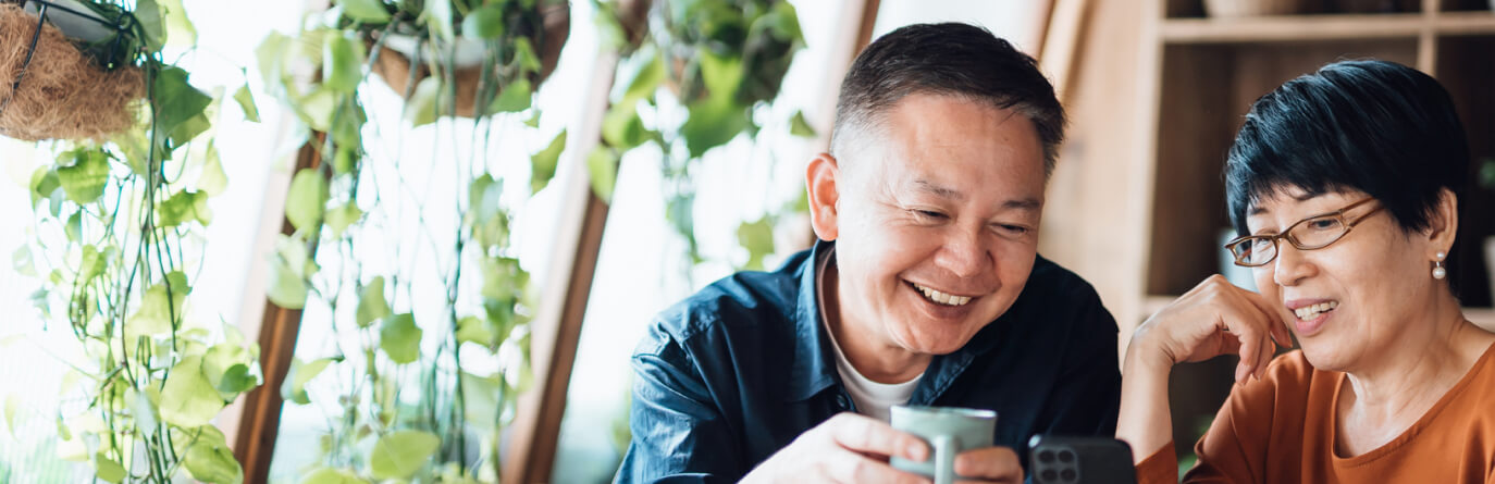 couple smiling while drinking coffee and using mobile phone