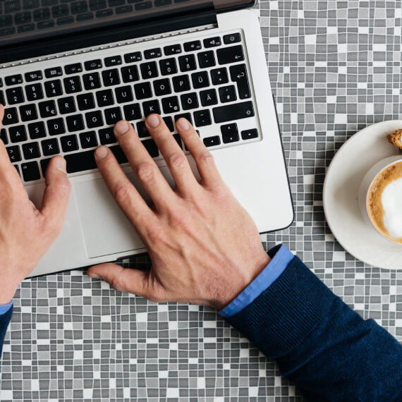 hands typing on a keyboard with a coffee