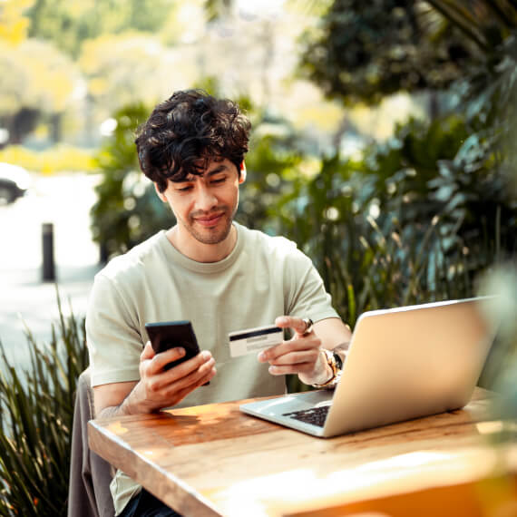 man holding phone and card in hand at an outdoor table